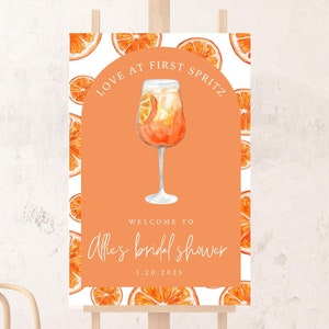 Op de afbeelding: Een oranje en wit bruidsdouchebord met een aquarel-illustratie van een glas Aperol Spritz. Het bord staat er "Love at First Spritz" en "Welkom bij Allie's bruidsdouche 1.20.2025".