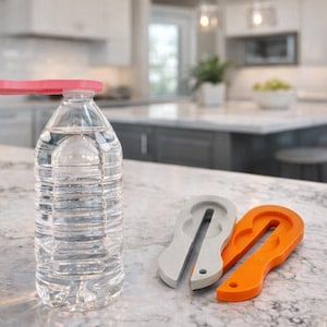 May include: A clear plastic water bottle filled with water, topped with a pink cap. Two bottle opener tools, one gray and one orange, are next to the bottle. The items are on a countertop in a kitchen setting.