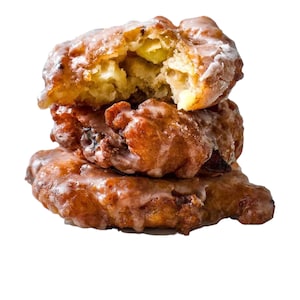 May include: A stack of three golden-brown apple fritters coated in a translucent white sugar glaze. The top fritter is broken open, revealing a soft, textured interior with visible pieces of cooked apple throughout the fried dough pastry.