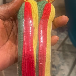 May include: A pair of long, colorful tassel earrings with green, red, and yellow yarn. The earrings are attached to a clear plastic backing and have a clear crystal bead with a red crystal bead at the top.