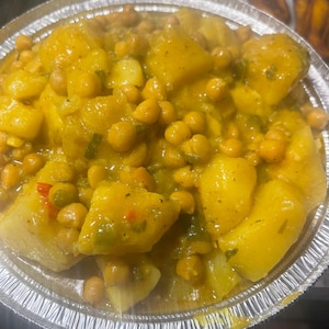 Puede incluir: Primer plano de un plato de garbanzos amarillos y patatas en un recipiente de aluminio plateado. Los garbanzos y las patatas están en una salsa cremosa amarilla.