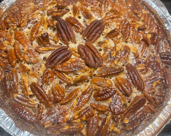 Könnte beinhalten: Ein frisch gebackener Pekannusskuchen in einer silbernen Folienform. Der Kuchen ist mit einer reichhaltigen, braunen Füllung gefüllt und mit ganzen Pekannüssen belegt. Der Teig ist goldbraun und der Kuchen scheint frisch gebacken zu sein.
