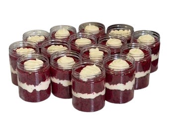 May include: A collection of fourteen clear plastic jars filled with layers of deep red cake and white frosting. Each jar features a visible middle layer of white cream and a decorative swirl of white frosting on the top surface.