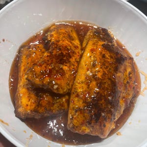 Può includere: Una ciotola bianca piena di tre pezzi di salmone cotto in una salsa marrone rossastra. Il salmone ha un colore arancione dorato con condimenti marrone scuro. La salsa ha un aspetto lucido.