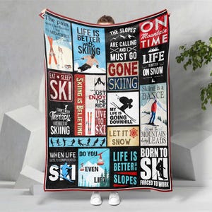 May include: A large, rectangular blanket with a black border and a collage of skiing-themed graphics and text. The blanket features various phrases like "Life is better with skiing" and "Skiing is a dance" in a mix of fonts and colors. The overall design is a tribute to the sport of skiing.