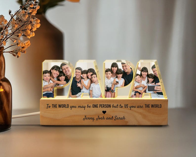 K&ouml;nnte beinhalten: Ein beleuchtetes Holzschild, das "PAPA" buchstabiert, mit einem Familienfoto in jedem Buchstaben. Das Schild tr&auml;gt die Botschaft "F&uuml;r die Welt bist du vielleicht nur eine Person, aber f&uuml;r uns bist du die Welt." und ist mit den Namen "Jenny, Josh und Sarah" personalisiert.
