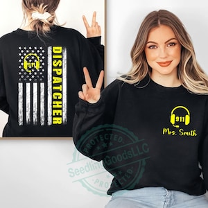 Puede incluir: Sudadera negra de manga larga con un diseño de despachador 911 amarillo. El diseño incluye un gráfico de auriculares y el texto "911 Sra. Smith" en la parte delantera. La parte posterior de la sudadera muestra un diseño de bandera estadounidense con la palabra "DISPATCHER".