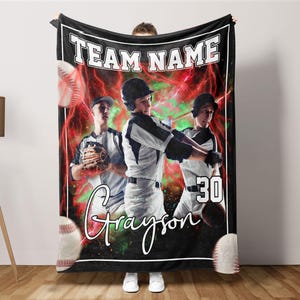 May include: A black baseball blanket with the text "TEAM NAME" and "Grayson" in white. The design includes baseball players and baseballs, set against a red and green backdrop. The number 30 is also visible.