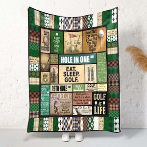 May include: A golf-themed quilt featuring various squares with golf-related text and imagery. The quilt has a patchwork design with green, brown, and white patterns. Text includes "Hole in One," "Eat. Sleep. Golf," and "Golf is Life."