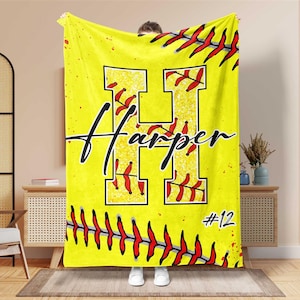 May include: A yellow softball-themed blanket with a large letter "H" in the center, filled with a textured design and red stitching. The name "Harper" is written in black script, and the number "12" is in the bottom right corner.