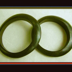 May include: Two dark green, oval-shaped bangles are interlocked, set against a light background. The bangles appear to be made of a solid material, possibly stone or a similar substance. The image is framed with a black border.