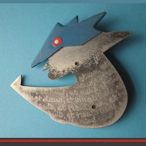 May include: Abstract metal sculpture with a blue, pointed top and a silver-colored body. The blue section has a red dot. The body has etched text and two small rivets. The sculpture is set against a blue background.