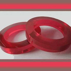 May include: Two transparent, red, oval-shaped bangles. The bangles are made of a solid material and have a smooth, polished surface. The bangles are displayed on a white surface, with a red and brown border.