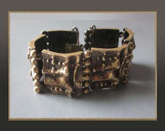 May include: A vintage gold-toned bracelet with a textured, brutalist design. The bracelet is composed of rectangular links with irregular surfaces and small, spherical accents. The links are connected by small, dark-colored hinges.