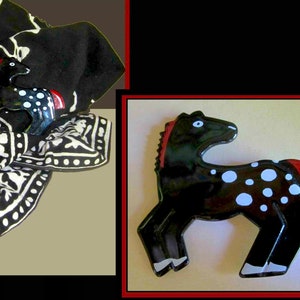 May include: A black horse figurine with white spots and a red mane and tail. The horse is displayed on a black and white patterned scarf. The figurine has a glossy finish and is a decorative item.