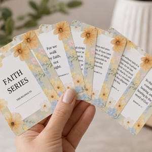 May include: A set of rectangular cards arranged in a fan shape, featuring a white center with black text and a floral border of yellow and blue flowers. The text includes the words FAITH SERIES and various religious verses printed on each card.