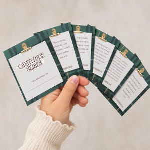 May include: A set of small cards with a dark green plaid pattern, each featuring a gold metal clip at the top. The cards display printed text including the title Gratitude Series and various scripture verses such as Psalm 118:24 and Daniel 2:23.
