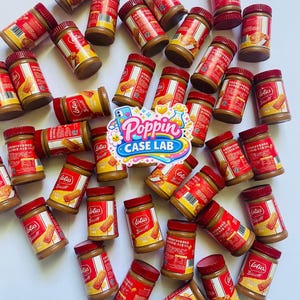 May include: A collection of small jars of Lotus Biscoff spread with red lids and labels, scattered across a white surface. A central sticker features the colorful text Poppin CASE LAB with a rainbow and cartoon icons, partially obscuring the jars.
