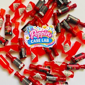 May include: A collection of miniature red hot sauce bottles, including Tabasco brand and other varieties, scattered around a central sticker featuring the text Poppin CASE LAB with colorful graphics of a smartphone, a flower, and a beaker.