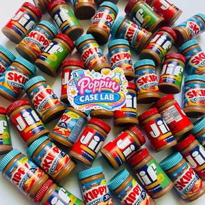 May include: A collection of miniature jars of Jif and Skippy creamy peanut butter with blue lids, scattered across a white surface. A colorful sticker with the text Poppin Case Lab is placed in the center of the arrangement of small jars.