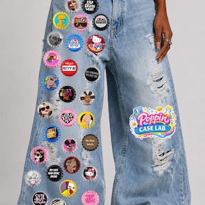 Puede incluir: Vaqueros anchos de mezclilla azul claro desgastados, adornados con numerosos broches de chapas de botella coloridos con varios estampados gráficos y textos. El texto BOTTLE CAP BROOCH SETS aparece arriba y Poppin CASE LAB en la pierna derecha.