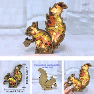 May include: A wooden squirrel figurine with a light-up feature. The squirrel is holding a nut in its paws and has a detailed design of leaves and mushrooms. The figurine is 6.29 inches tall and 5.51 inches wide. The back of the figurine can be personalized with custom text.
