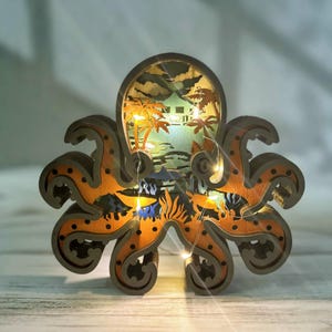 以下が含まれることがあります： 木製のタコ彫刻で、内部にライトアップされたシーンがあります。シーンは、ヤシの木と家のあるビーチです。タコはオレンジと茶色に黒のドットでペイントされています。