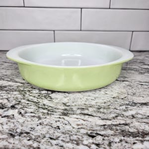 Puede incluir: Un plato redondo verde claro y blanco con un borde ligeramente elevado. El plato tiene un acabado liso y brillante, posiblemente de cerámica o vidrio. El interior es blanco y el exterior es de color verde pálido.