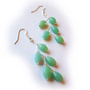 May include: A pair of silver dangle earrings with light green oval-shaped beads. The beads are arranged in a cascading pattern, resembling branches with leaves.