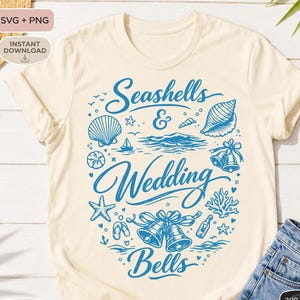 May include: Cream-colored t-shirt with a blue graphic design featuring seashells, waves, and wedding bells. The text reads "Seashells & Wedding Bells". The design includes nautical elements like starfish and a sailboat.