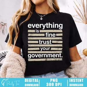 Puede incluir: Camiseta negra con la frase "everything is fine trust your government" en fuente blanca desgastada. El texto está dispuesto en forma apilada con rayas horizontales. La camiseta tiene cuello redondo y mangas cortas.