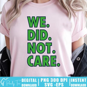 Puede incluir: Camiseta rosa claro con la frase "WE. DID. NOT. CARE." en letras verdes. El texto está delineado en verde oscuro. La camiseta tiene mangas cortas y cuello redondo.