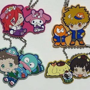 Op de afbeelding: Een set van tien kleurrijke sleutelhangers met cartoonfiguren. De sleutelhangers zijn gemaakt van rubber en hebben verschillende ontwerpen, waaronder een meisje met rood haar, een roze konijn, een gele hond, een blauw monster, een meisje met bruin haar en een jongen met oranje haar.