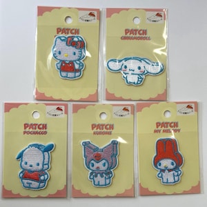 Op de afbeelding: Vijf kleurrijke strijklabels met populaire Sanrio-personages: Hello Kitty, Cinnamoroll, Pochacco, Kuromi en My Melody. Elk strijklabel bevindt zich op een witte kaart met Japanse tekst.