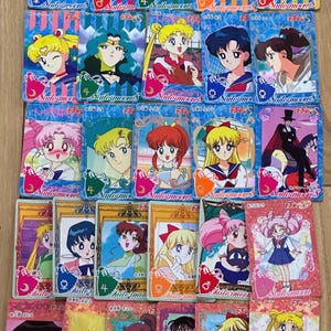 Op de afbeelding: Een verzameling Sailor Moon-verzamelkaarten. Elke kaart toont een ander personage uit de animeserie, met levendige kleuren en gedetailleerde illustraties. De kaarten hebben een rechthoekige vorm en zijn in een raster gerangschikt.