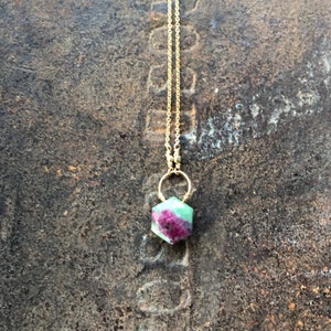 May include: A gold chain necklace with a green and pink gemstone pendant. The pendant is a hexagonal shape and is wrapped in gold wire.
