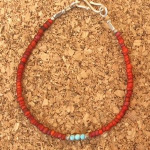 May include: A red beaded bracelet with a silver clasp and three turquoise beads.