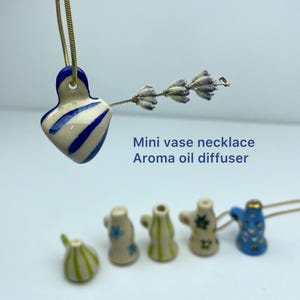 May include: A small ceramic vase pendant with blue and white stripes, suspended on a gold chain, holding a sprig of dried lavender. The image also shows other miniature vase pendants. The text reads: Mini vase necklace Aroma oil diffuser.