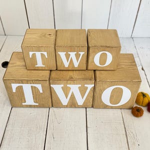 May include: Wooden blocks spelling out the word "TWO" in white letters. The blocks are stacked in two rows, with the top row spelling out "TWO" and the bottom row spelling out "TWO".