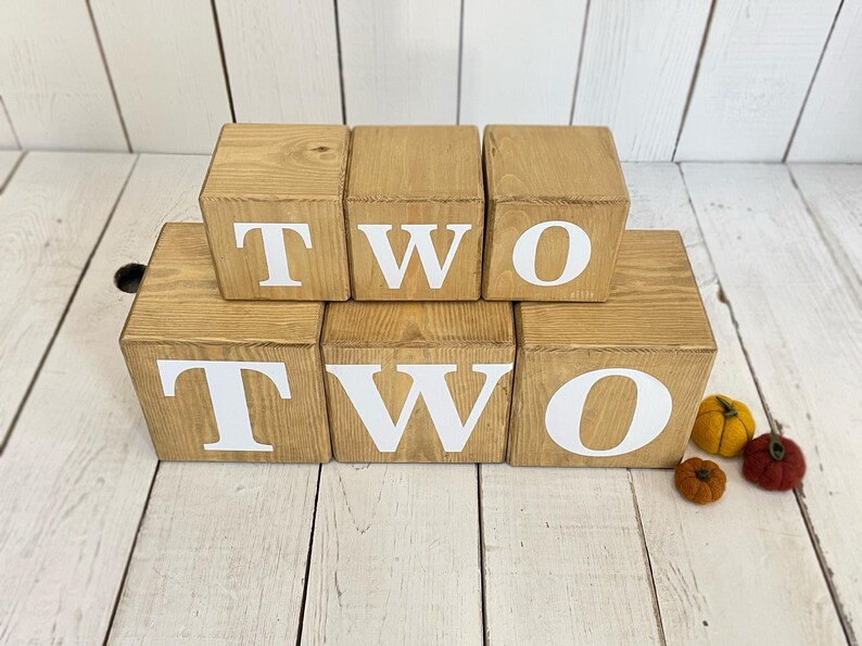May include: Wooden blocks spelling out the word "TWO" in white letters. The blocks are stacked in two rows, with the top row spelling out "TWO" and the bottom row spelling out "TWO".
