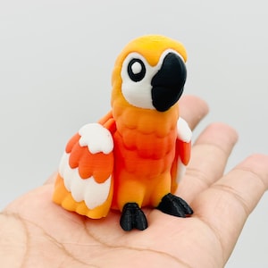 May include: A 3D-printed orange and white parrot figurine with a black beak and feet. The parrot has large, round eyes and is perched on a hand. The figurine is a decorative item.