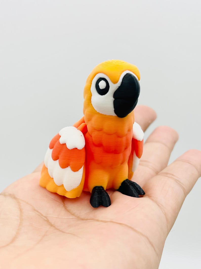 May include: A 3D-printed orange and white parrot figurine with a black beak and feet. The parrot has large, round eyes and is perched on a hand. The figurine is a decorative item.