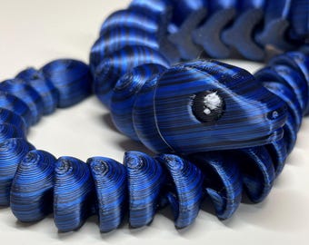 May include: A blue and black patterned snake-shaped bracelet made of plastic. The bracelet is coiled and has a snake head with a white eye.