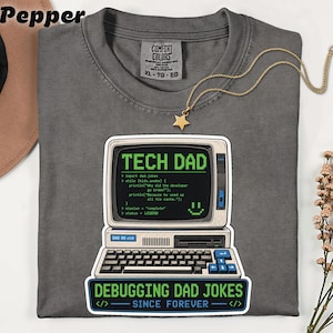 May include: Pepper-colored Comfort Colors t-shirt with a graphic of a retro computer screen that says "TECH DAD" and "Debugging Dad Jokes Since Forever." The shirt has a gold star necklace.