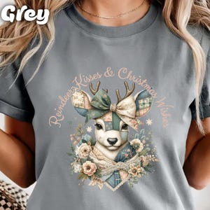 May include: Grey t-shirt featuring a watercolor illustration of a reindeer with patchwork ears and a bow. The text "Reindeer Kisses & Christmas Wishes" is arched around the reindeer. The reindeer is surrounded by floral elements.