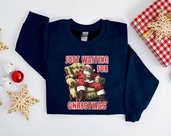 May include: A navy blue sweatshirt with a graphic of Santa Claus sitting in a chair and the text "Just Waiting for Christmas".