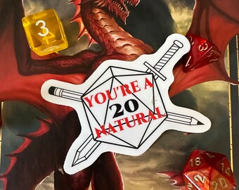 May include: A sticker with the text "YOU'RE A 20 NATURAL" is centered on a book cover featuring a red dragon illustration. Several dice, including a D20, are scattered around the sticker, suggesting a tabletop gaming theme.