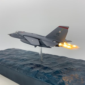 以下が含まれることがあります： 尾番号「522」と尾部に「CC」の文字が書かれた灰色の飛行機の模型。飛行機はアフターバーナーを点灯させて青い海の上を飛んでいる。