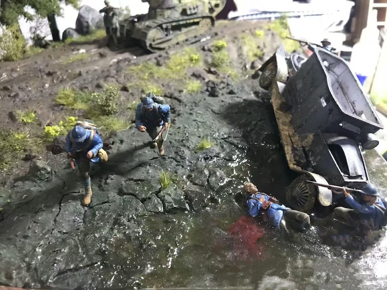 May include: A detailed diorama depicting a war scene with miniature soldiers in blue uniforms, a tank, and a vehicle overturned in a muddy environment. The scene includes water and vegetation, creating a realistic battlefield.