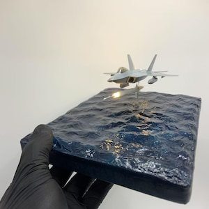 Diorama do modelo de caça a jato Lockheed Martin/Boeing F-22 Raptor em escala 1:144, com efeitos de iluminação lançados pelo AIM-120 AMRAAM